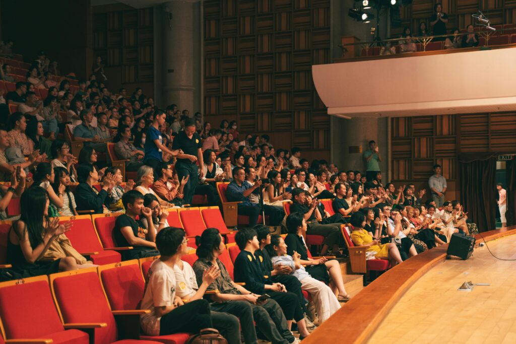 A lively audience applauding in a spacious concert hall, creating energy and excitement.