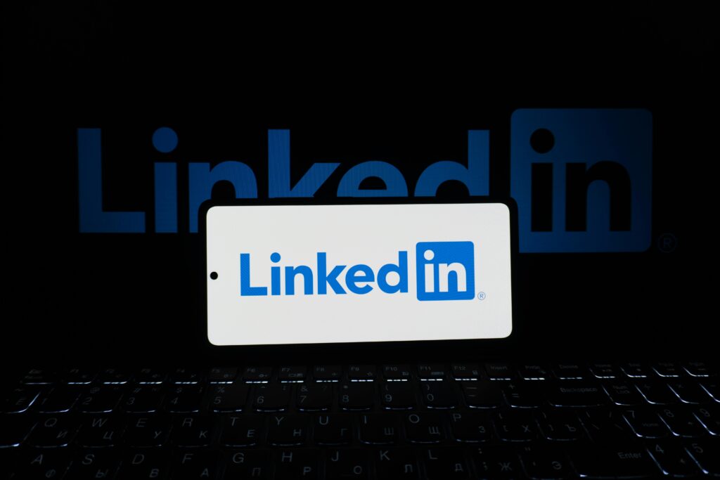 Smartphone showing LinkedIn logo with keyboard and large background logo, business theme.