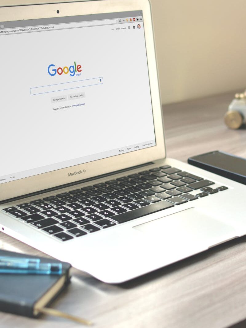 A neat workspace featuring a laptop displaying Google search, a smartphone, and a notebook on a wooden desk.